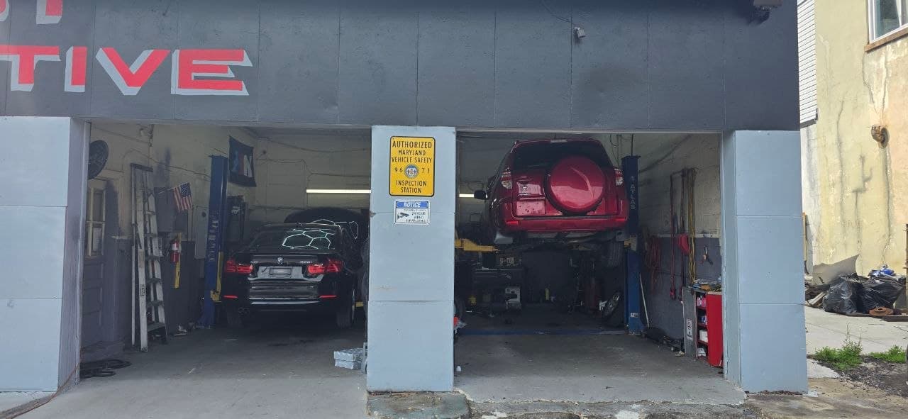 Two service bays with cars on the lifts and the authorized Maryland inspection station sign on the center pillar